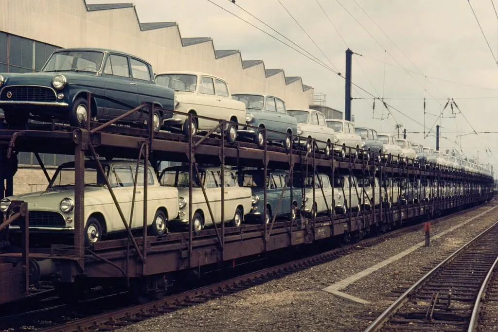1960s double-deck Cartic-4 style railway wagons loaded with rows of new British cars at an industrial rail yard