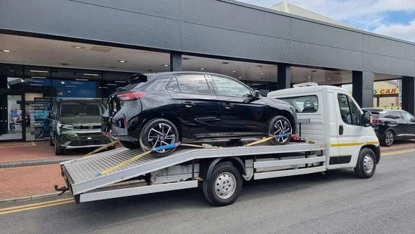 Black car securely loaded on transport trailer with straps in UK