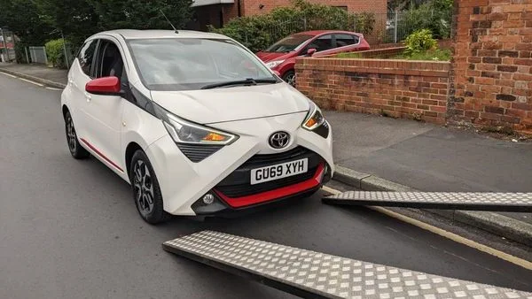 White Toyota car being loaded onto transport ramp in UK street